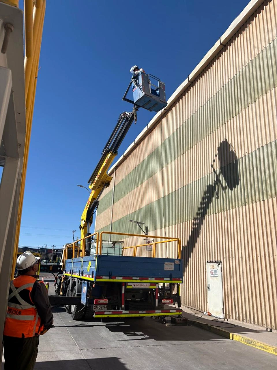 Camión pluma en acceso industrial. Equipo desplegado en corredor de acceso para trabajo en altura.