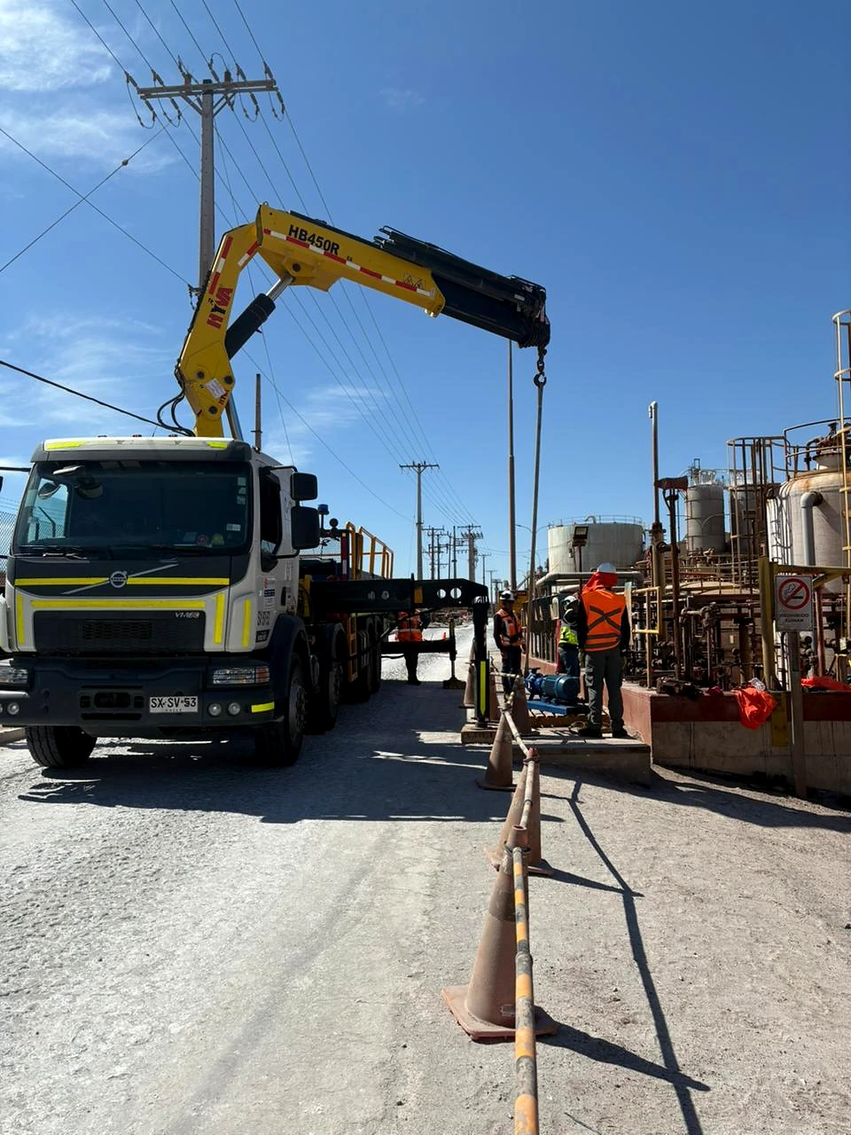 Apoyo operacional en vía industrial. Camión pluma preparado para maniobras junto a infraestructura de planta.