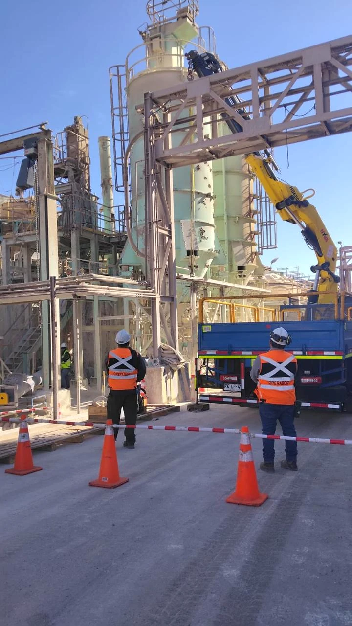 Camión pluma al interior de planta. Trabajo de izaje en instalación industrial con demarcación de seguridad.