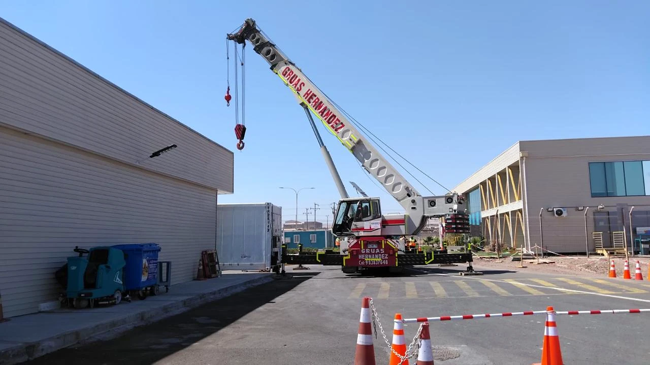 Grúa telescópica en operación industrial. Maniobra de izaje de largo alcance con área de trabajo controlada.